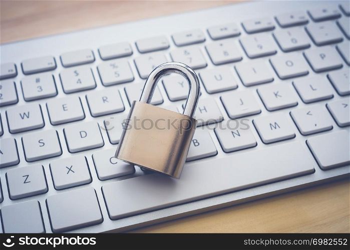 Close key padlock on white keyboard, wooden table background, dark vintage retro. System access, encryption, online internet, password cracking, blockchain, cyber security, information protection.