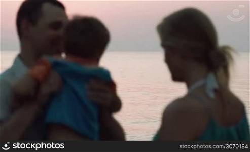 Close-knit family of three on the beach. Father holding son, they come closer to each other. Boy kissing his parents