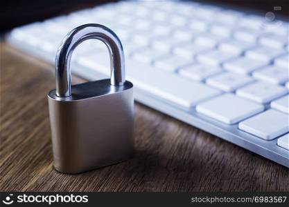 Close metal padlock with and modern white keyboard on wooden table, dim light dark tone background. Digital data protection, encryption, internet access, cyber network, password security concepts.