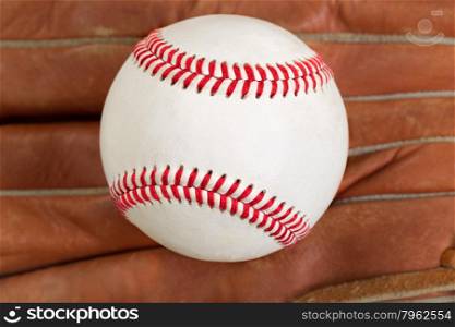 Close of baseball, selective focus on center, with leather mitt in background. Format in filled frame layout.