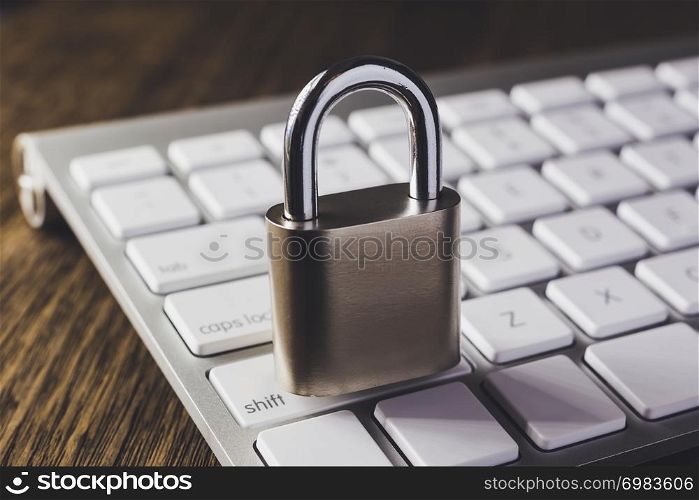Close padlock key on modern white keyboard with wooden table on background, dim light dark tone. Digital data protection, internet access, cyber network, password security, online business concepts.