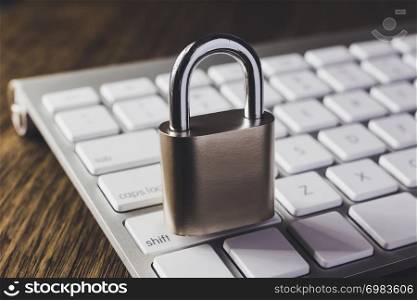 Close padlock key on modern white keyboard with wooden table on background, dim light dark tone. Digital data protection, internet access, cyber network, password security, online business concepts.