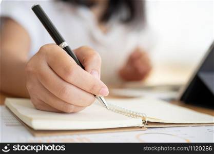 Close shot of businesswoman hands holding a pen writing something on the paper on the foregroundin office. Recording concept