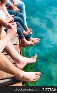 Close shot of legs family spending time together sitting on jetty over the lake in the summertime