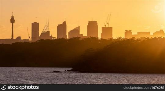 Close silhouette view of Sydney downtown with trees in the foreground. Sun rays spreading an amazing orange color cast over the trees. Beautiful orange sky in the background