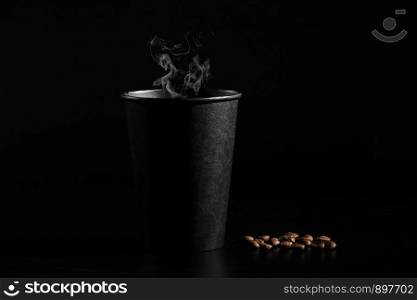 close-up. A black glass of hot coffee with scattered coffee beans on a black background.. A black glass of hot coffee with scattered coffee beans on a black background. close-up