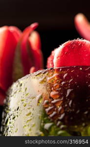 Close up a buds red tulips with water drops in a green glass on a black background. Fine art floral background. Macro.. Close up a buds red tulips with water drops in a green glass on a black background.