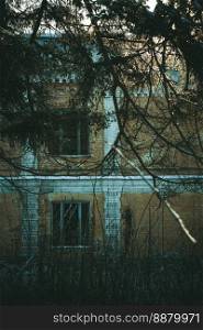 Close up abandoned multi storey building with overgrown fir branches concept photo. Front view photography with blurred background. High quality picture for wallpaper, travel blog, magazine, article. Close up abandoned multi storey building with overgrown fir branches concept photo
