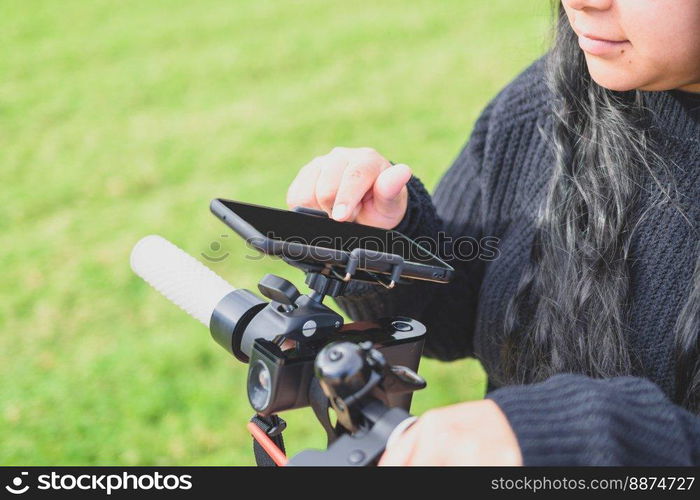 close-up and cropped view of beautiful latina woman with long hair and black clothes using smart phone apps riding motorised scooter in the city, mobility concept sustainable transport, zero CO2 emissions Emobility. young latina woman, using smartphone app to unlock electric scooter