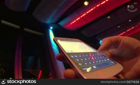 Close-up and wide angle shot of female hand texting on touschscreen smart phone at nightclub. Lighting changing colors