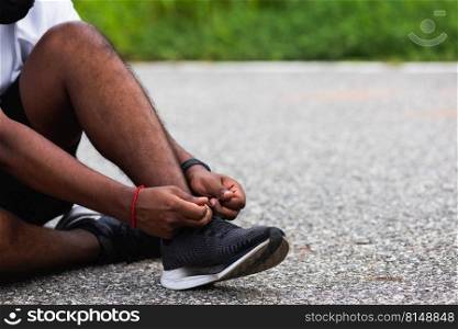 Close up Asian sport runner black man sitting shoelace trying running shoes getting ready for jogging and run at the outdoor street, health exercise workout concept