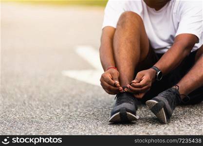 Close up Asian sport runner black man wear watch sitting he trying shoelace running shoes getting ready for jogging and run outdoor street health park with copy space, healthy exercise workout concept