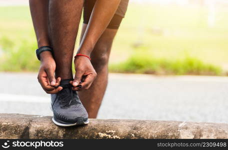 Close up Asian sport runner black man wear watch stand step on the footpath trying shoelace running shoes getting ready for jogging and run outdoor street health park, healthy exercise workout concept