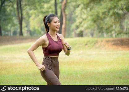 Close up Asian woman jogging in park or garden with green field and tree as background during morning time.
