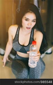 Close-up Asian women performing doing exercises training howing a bottle of water in sport gym interior and fitness health club with sports exercise equipment Gym background.