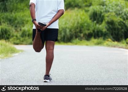 Close up Asian young athlete sport runner black man wear watch lift feet stretching legs and knee before running at the outdoor street health park, healthy exercise before workout concept