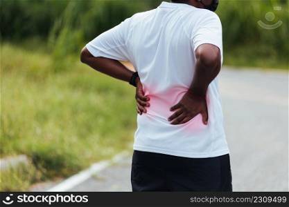 Close up Asian young sport runner black man wear watch feel pain on his spine low back and hip while running at the outdoor street health park, healthy exercise Injury from workout concept