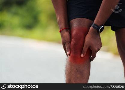 Close up Asian young sport runner black man wear watch stand use hands joint hold knee pain during the run while running at the outdoor street health park, healthy exercise injury from workout concept