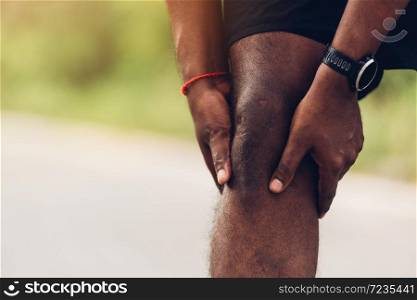 Close up Asian young sport runner black man wear watch stand use hands joint hold knee pain during the run while running at the outdoor street health park, healthy exercise injury from workout concept