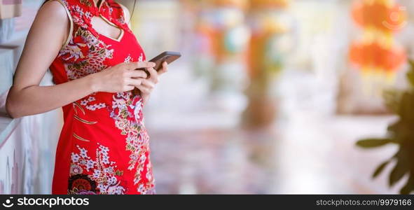 Close up Asian young woman wearing red traditional Chinese cheongsam decoration and writing message on smartphone for Chinese New Year Festival at Chinese shrine in Thailand