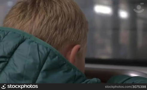 Close-up back shot of a child looking through the window of moving underground train