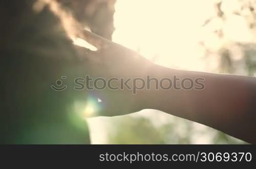 Close-up back view of a woman looking far way during sunset hiding herself from the sun with her hand