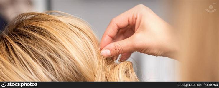 Close up back view of hand of female hairdresser makes hairstyle of young blonde woman in beauty salon. hairdresser makes hairstyle of young woman