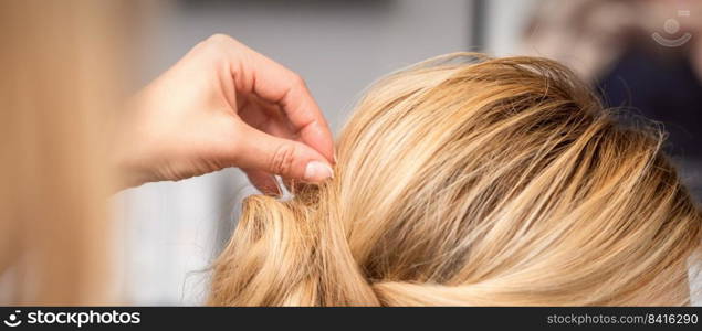 Close up back view of hand of female hairdresser makes hairstyle of young blonde woman in beauty salon. hairdresser makes hairstyle of young woman