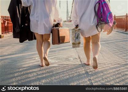 Close up barefoot women with suitcases walking across bridge concept photo. Back view photography with blurred background. High quality picture for wallpaper, travel blog, magazine, article. Close up barefoot women with suitcases walking across bridge concept photo