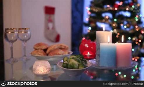 Close up beautiful festive table setting and candles burning by Christmas tree with lights at the background.