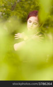 Close-up - beautiful makeup girl wearing black tunic and an antique jewels, green leaves around