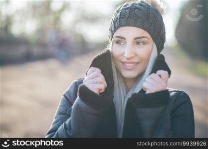 Close-up beautiful young woman with smile face in warm clothing on winter day outdoors. Happy girl wearing wool cap and black jacket.Female person in cold weather.