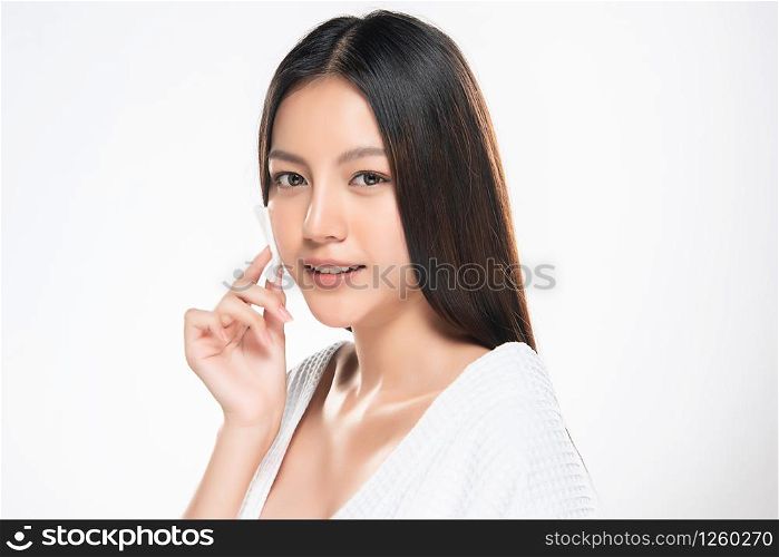 Close up beauty portrait of a young attractive woman cleaning her face with a cotton pad isolated over white background