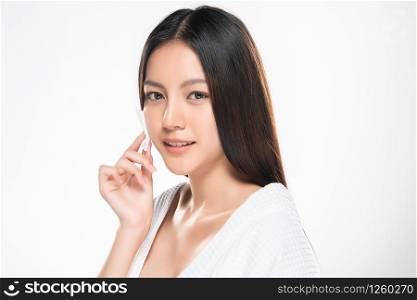 Close up beauty portrait of a young attractive woman cleaning her face with a cotton pad isolated over white background