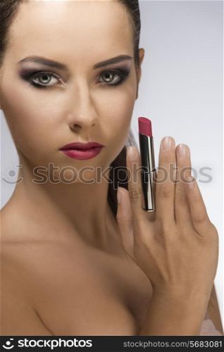 close-up beauty portrait of very pretty brunette lady taking purple lipstick in the hand and posing with stylish make-up and perfect clean skin