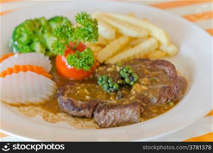close up beef steak with green peppercorn sauce served with vegetable and french fries . beef steak