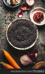 Close up black lentils in bowl with ingredients for delicious cooking. Top view. Copy space. Healthy food. Protein rich vegan foods. Plant based protein source