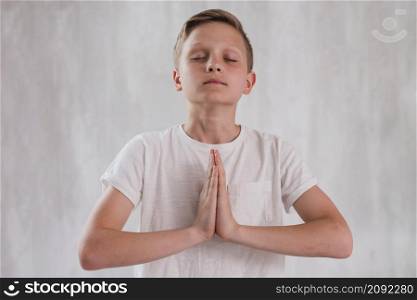 close up boy closing his eyes doing meditation against concrete wall