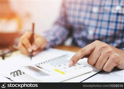 Close up business man hand is writing in a notebook and using calculator counting making notes Accounting at doing finance at office. Savings finances concept. note pad