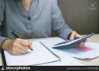 Close up businessman hand using calculator and writing in a notebook counting making notes Accounting at doing finance at home office. Savings finances concept. note pad