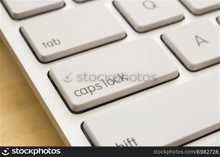 Close up caps lock button on white keyboard, wooden table on background. Computer technology, internet communication, e-commerce, online education concepts.