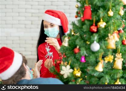 Close up Caucasian woman with hygiene mask decorate the Christmas tree with his couple in his home for celebrate the festival during pandemic of Covid-19 and new normal lifestyle.