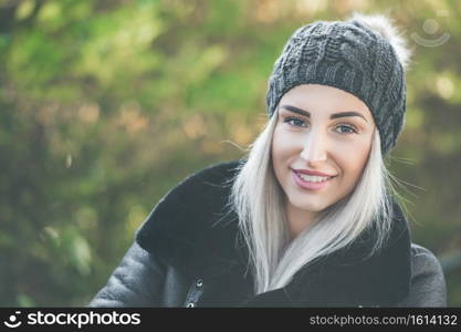 Close-up cheerful woman in warm clothing, winter day outdoors. Happy girl wearing wool cap and black jacket. Female person in cold weather.