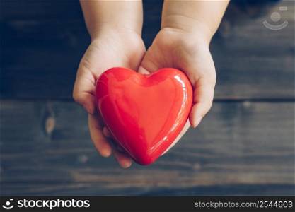 Close up children hands giving red heart on wood background