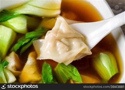 Close up Chinese wanton soup, single piece in spoon, with bok choy on rustic wood.