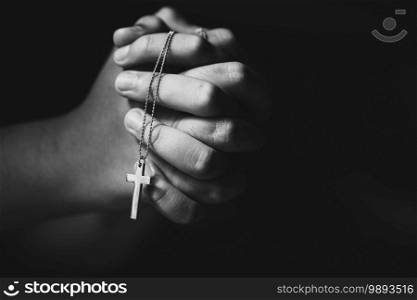 Close up christian hands holding cross while praying.