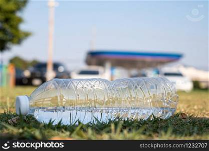 Close up clear plastic bottle water drink with a white cap on green field in the park at blurred background, litter on the ground in the garden, Trash that is left outside the bin