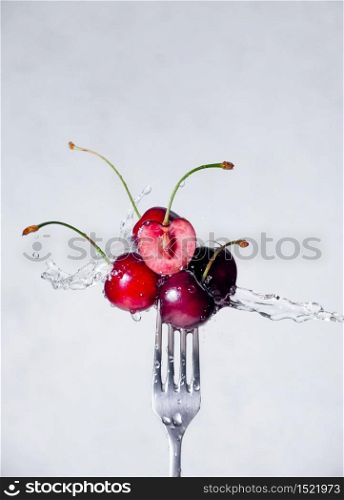 Close up Composition of Cherries on Fork Flying in the air with Water Splashes on the Light Grey Background.. Close up Composition of Cherries on Fork Flying in the air with Water Splashes on the Light Grey Background