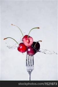 Close up Composition of Cherries on Fork Flying in the air with Water Splashes on the Light Grey Background.. Close up Composition of Cherries on Fork Flying in the air with Water Splashes on the Light Grey Background