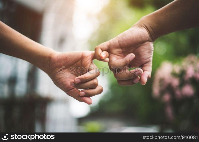 Close up couple holding pinkies fingers in park in autumn as swear and promise gesture in wedding ceremony. Hands holding of love Valentines day theme. Togetherness of friendship with green natural